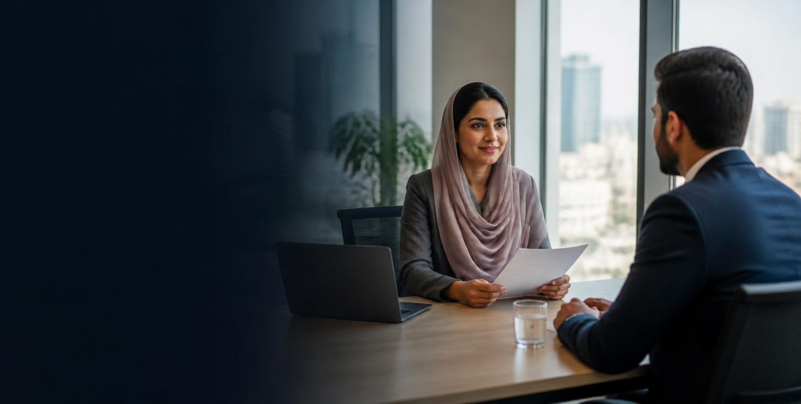 Recruiter in a Karachi office interviewing a candidate, holding his CV across a meeting table